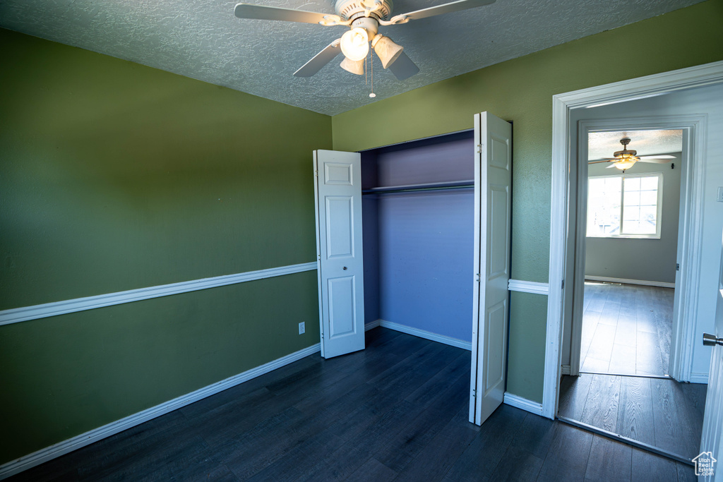 Unfurnished bedroom with dark wood finished floors, a textured ceiling, baseboards, a closet, and a ceiling fan