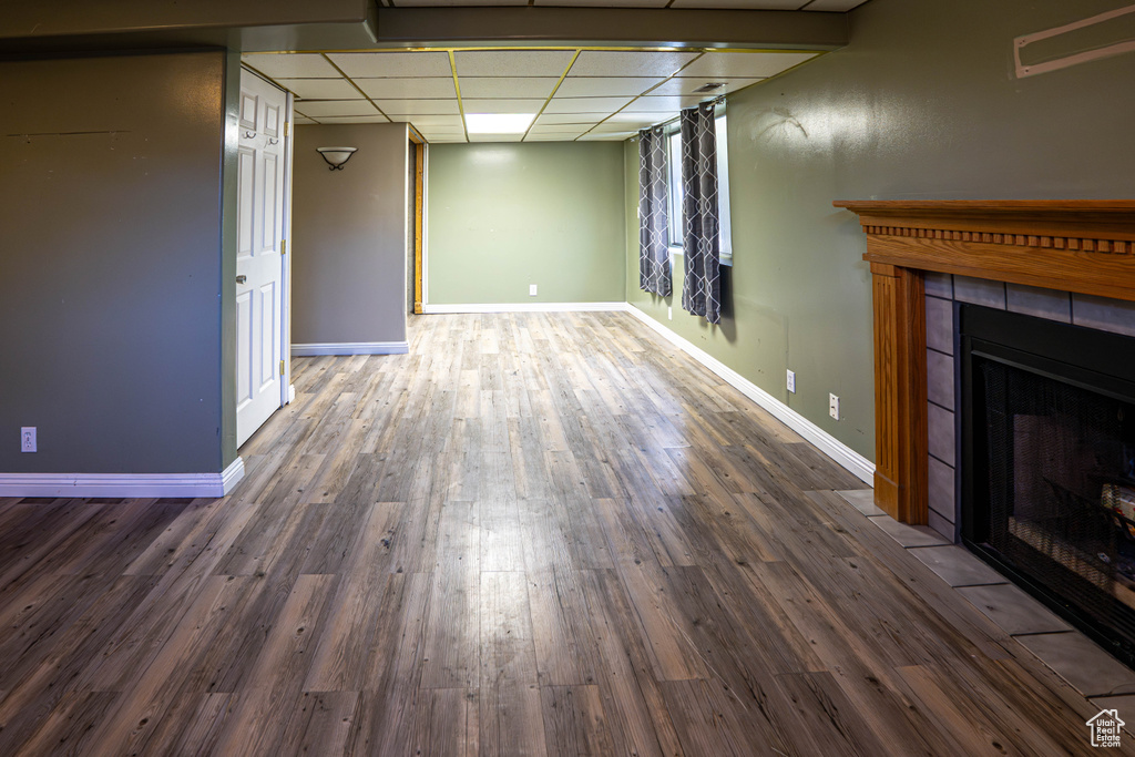 Unfurnished living room with a paneled ceiling, wood finished floors, a tile fireplace, and baseboards