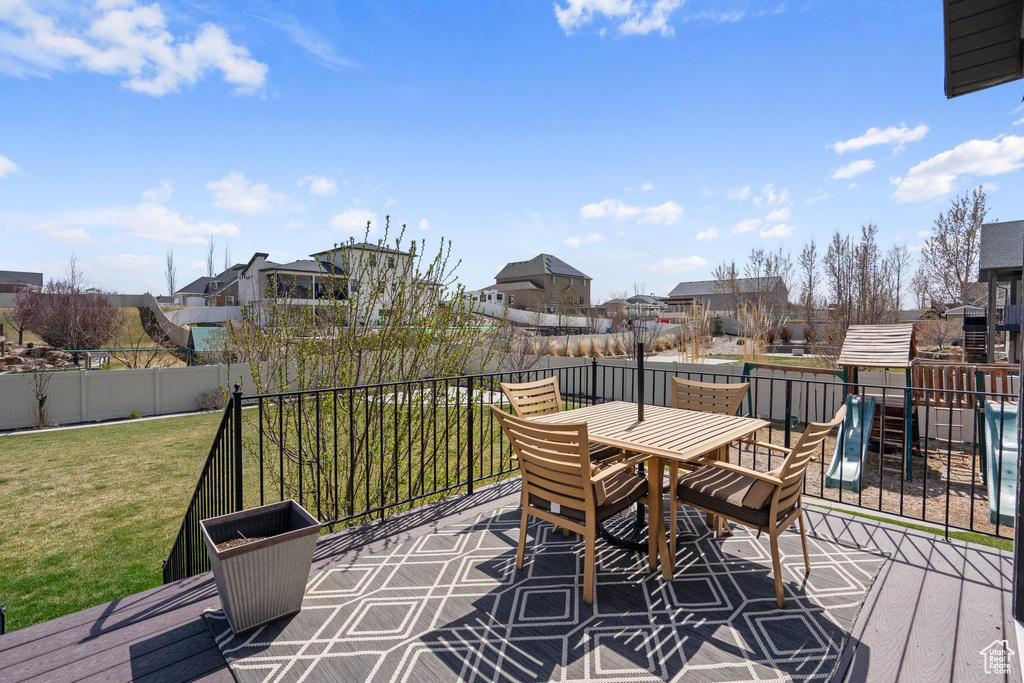 Wooden deck featuring outdoor dining area, a yard, fence, a playground, and a residential view