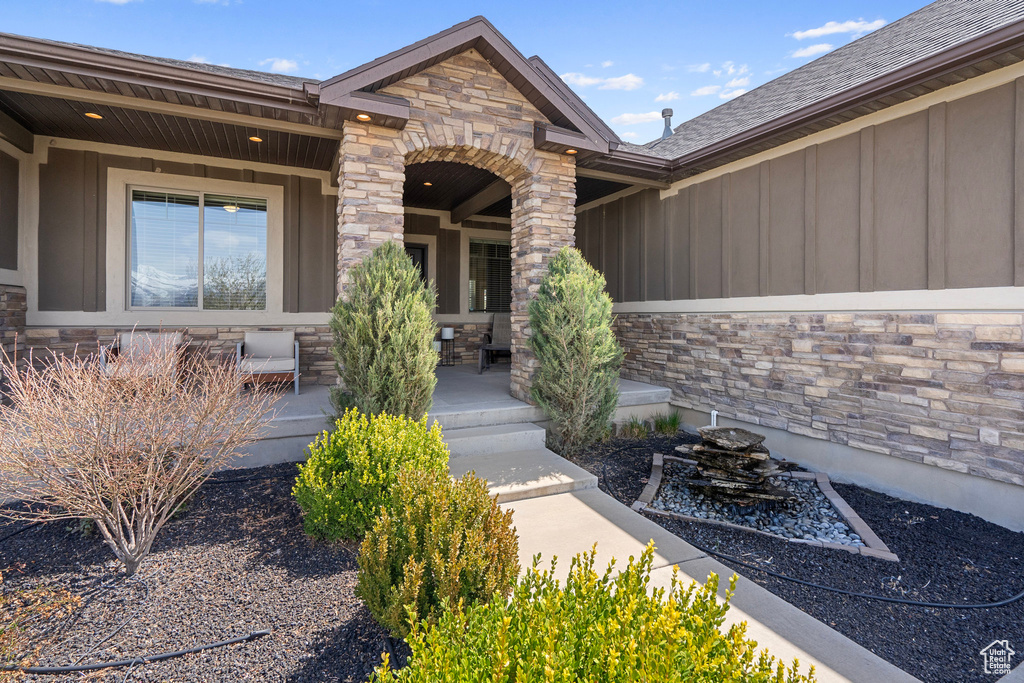 Doorway to property featuring board and batten siding, covered porch, and stone siding