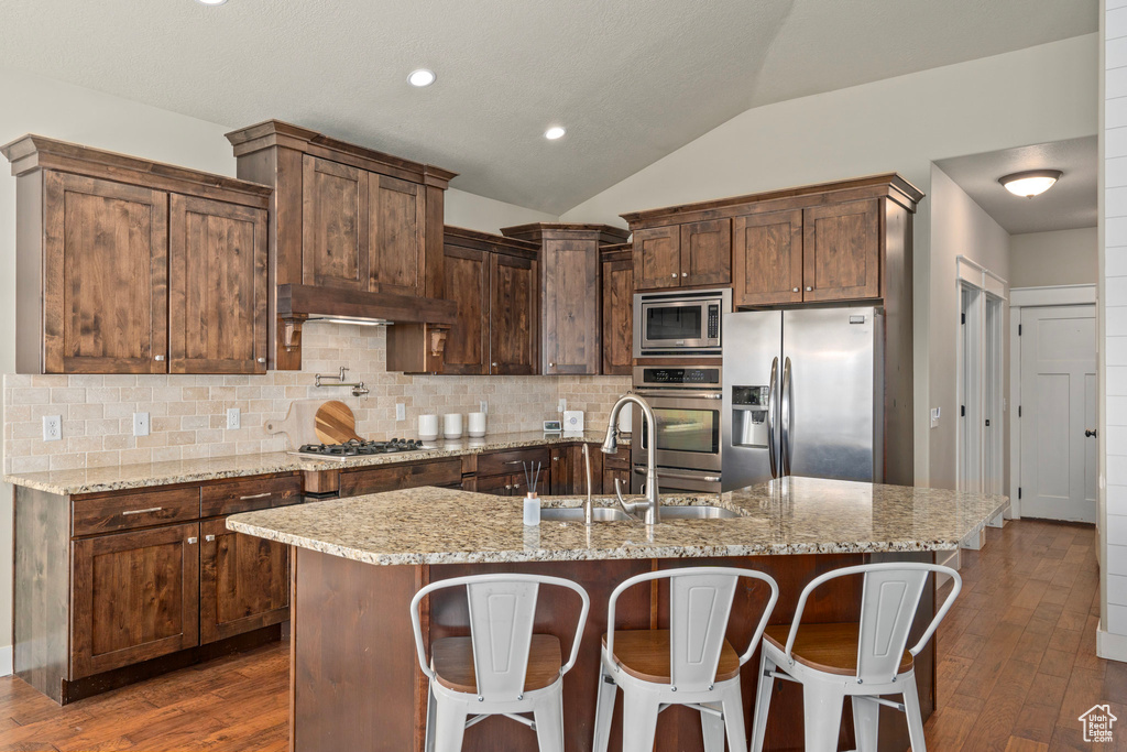 Kitchen featuring tasteful backsplash, a sink, appliances with stainless steel finishes, under cabinet range hood, and vaulted ceiling