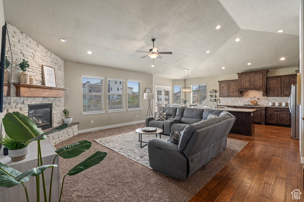 Living area featuring a stone fireplace, dark wood-style floors, a textured ceiling, a ceiling fan, and lofted ceiling