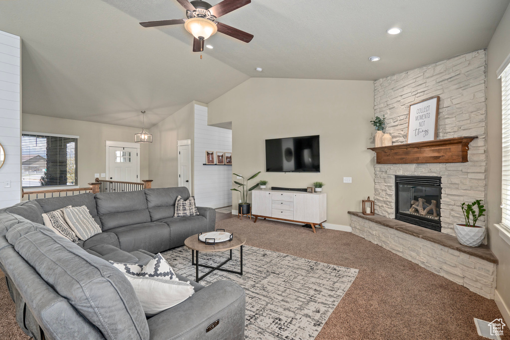 Carpeted living area featuring a ceiling fan, visible vents, a stone fireplace, vaulted ceiling, and baseboards