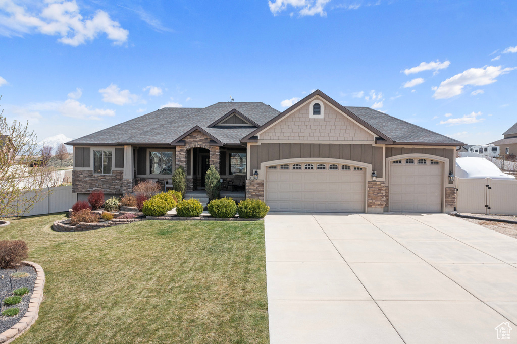 View of front of home with an attached garage, stone siding, fence, concrete driveway, and a front lawn