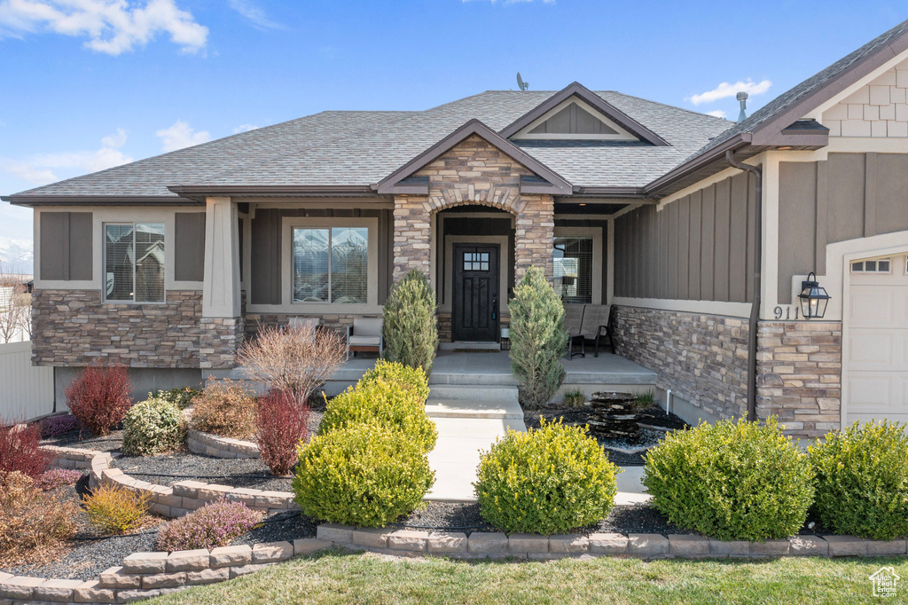 Craftsman-style house featuring roof with shingles, stone siding, an attached garage, and covered porch