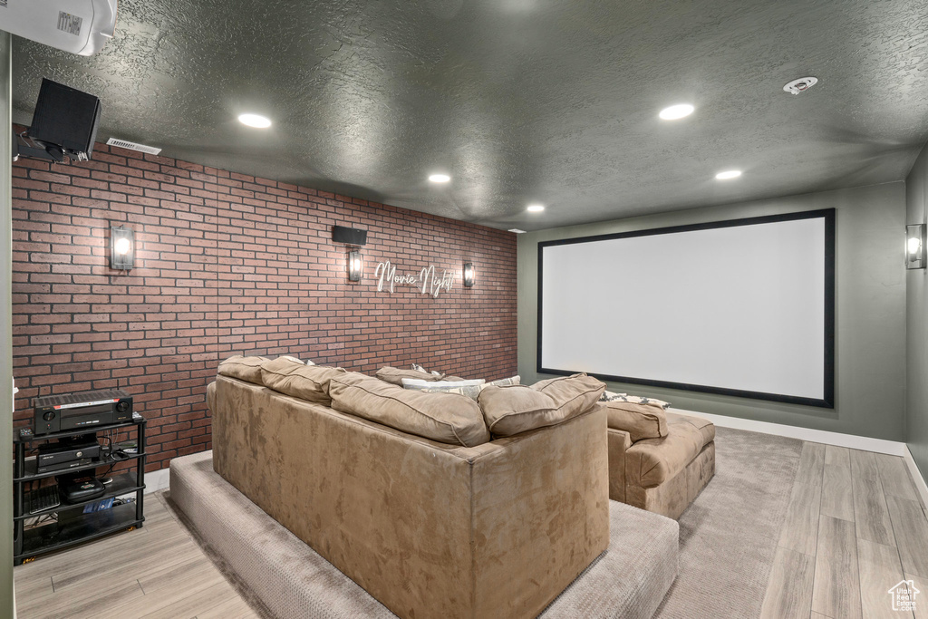 Home theater room with a textured ceiling, wood finished floors, brick wall, and recessed lighting