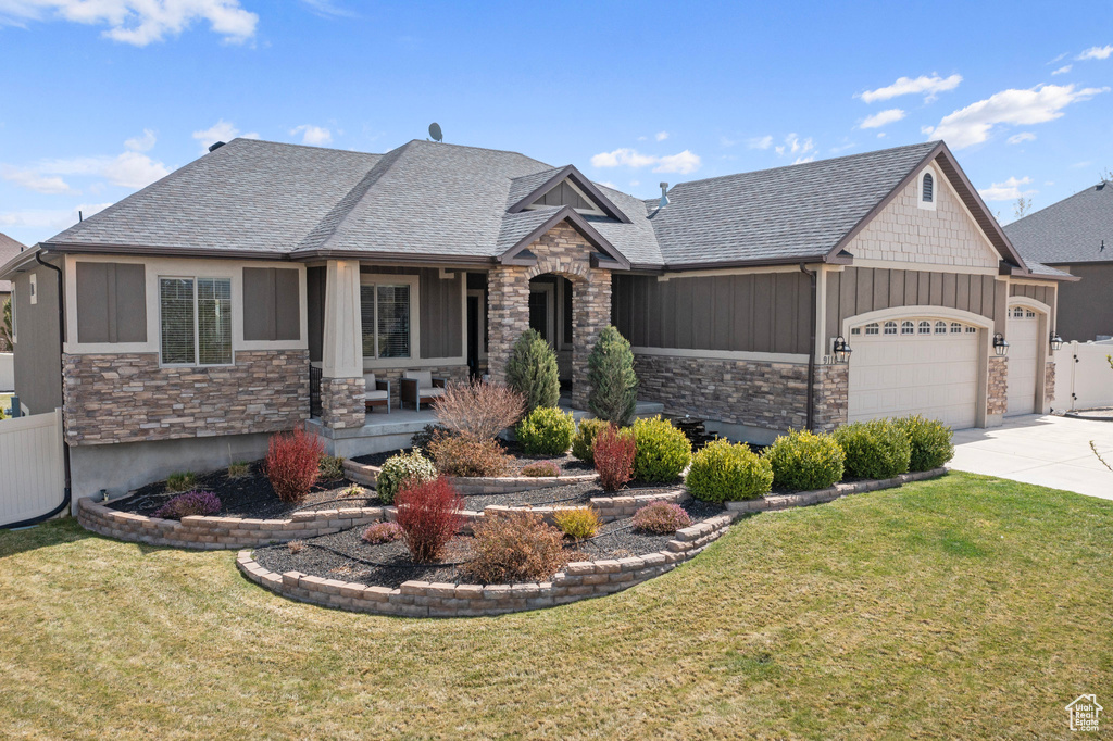 Craftsman-style house featuring concrete driveway, a front lawn, stone siding, and an attached garage
