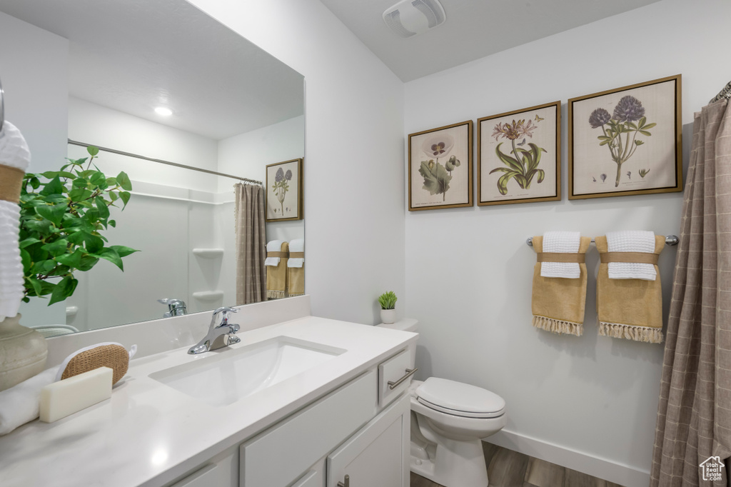 Bathroom with baseboards, a shower with curtain, toilet, vanity, and wood finished floors