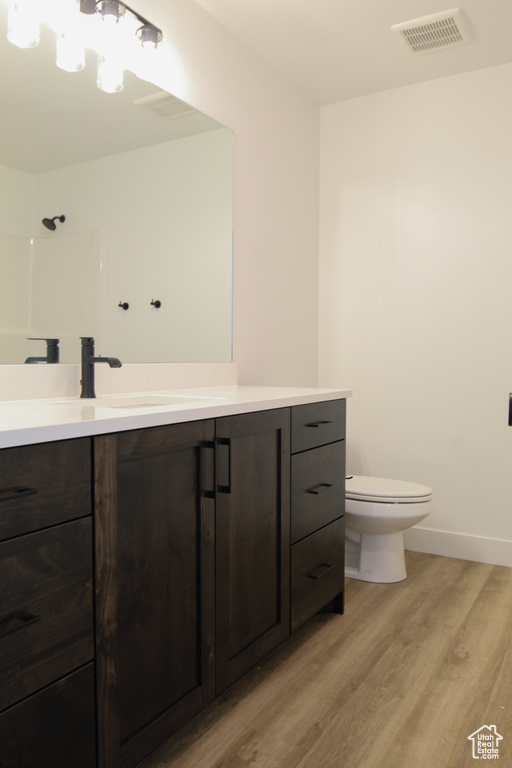 Bathroom with toilet, wood finished floors, vanity, visible vents, and baseboards