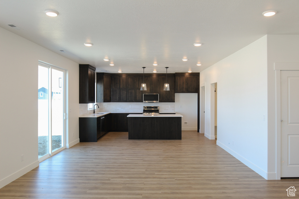 Kitchen featuring a sink, appliances with stainless steel finishes, baseboards, a kitchen island, and light wood-style floors