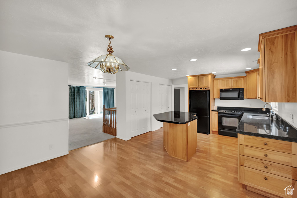 Kitchen with an inviting chandelier, a kitchen island, black appliances, light wood-style floors, and a sink