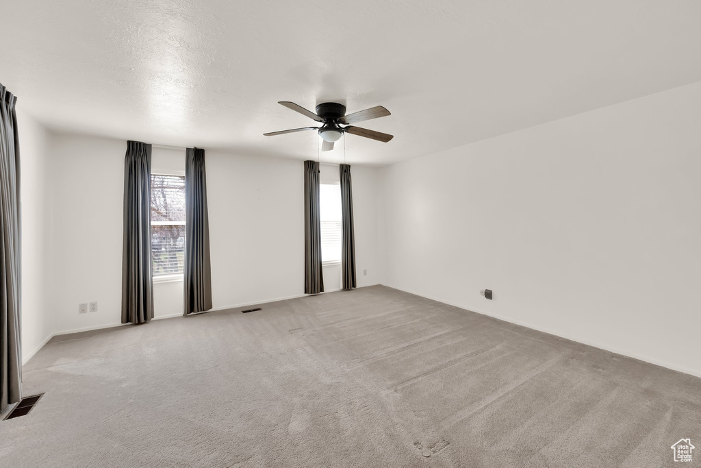 Empty room featuring carpet flooring, a ceiling fan, and visible vents