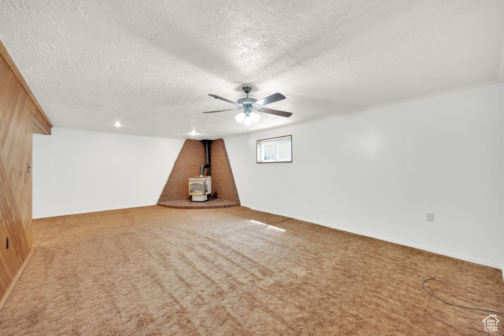 Interior space with carpet floors, a wood stove, a ceiling fan, and a textured ceiling