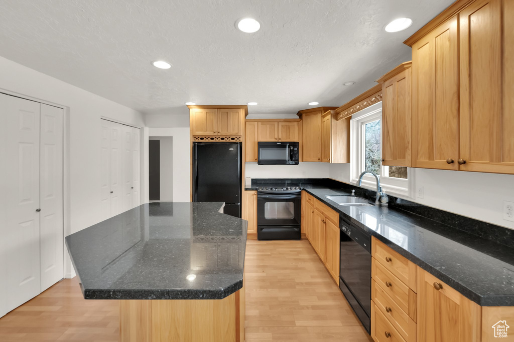 Kitchen with a sink, light wood-type flooring, black appliances, and a center island