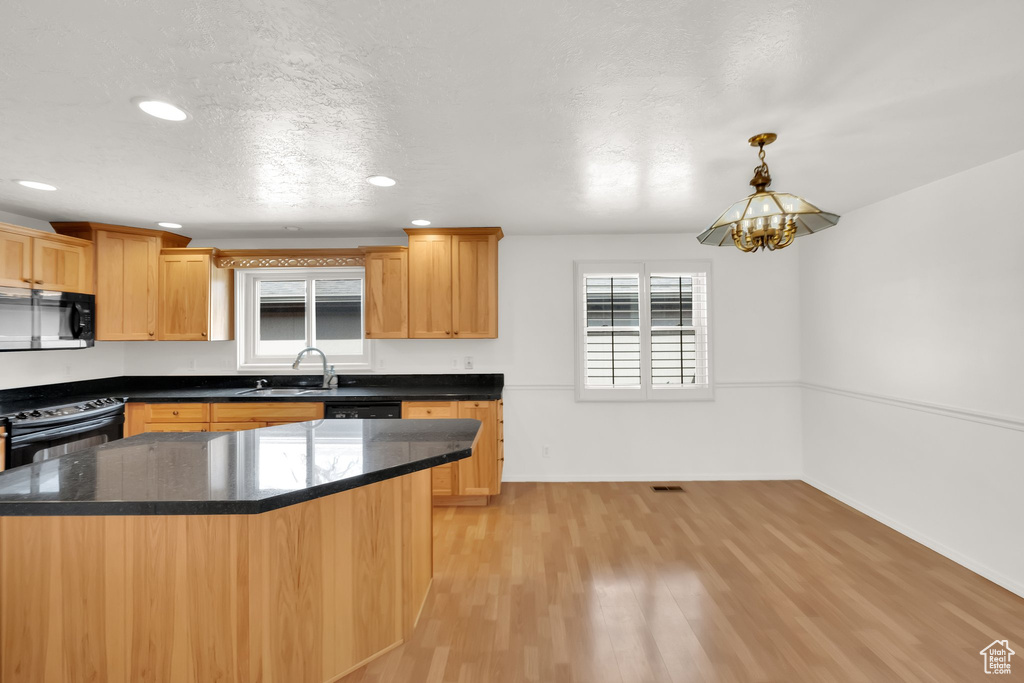 Kitchen with light wood-style flooring, a textured ceiling, black appliances, a sink, and baseboards