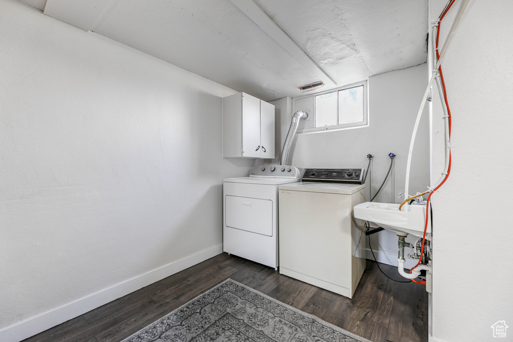 Washroom with baseboards, a sink, dark wood-style flooring, independent washer and dryer, and cabinet space