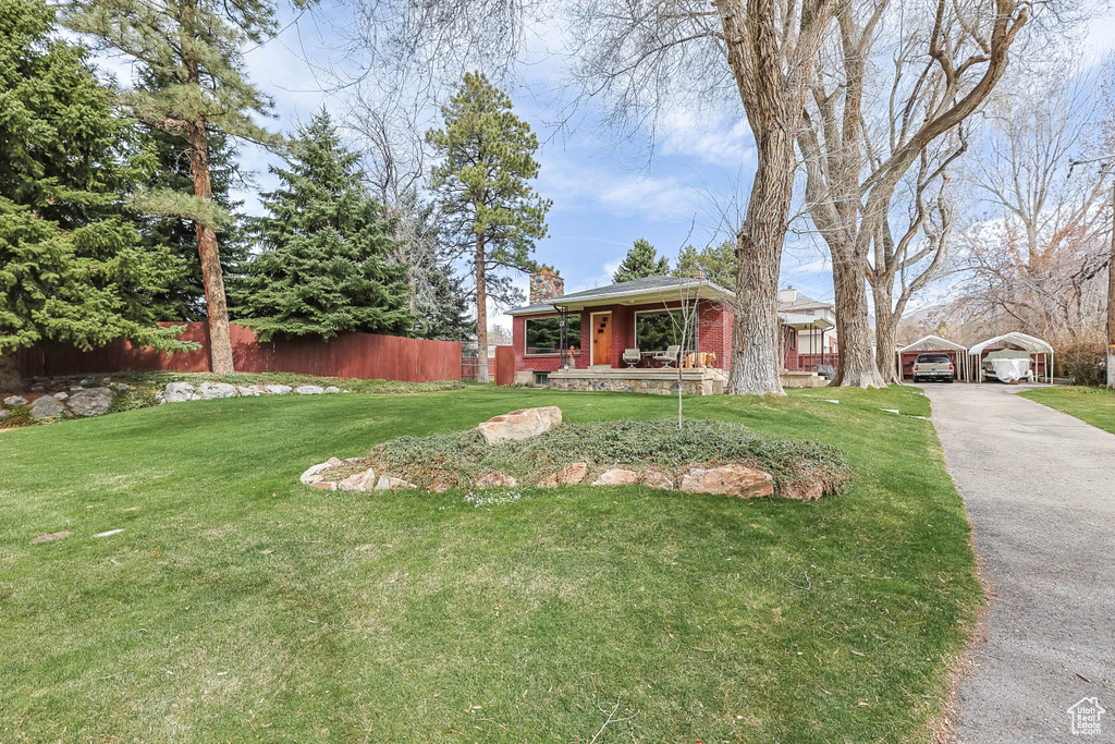 View of front of house with a carport, aphalt driveway, fence, and a front lawn