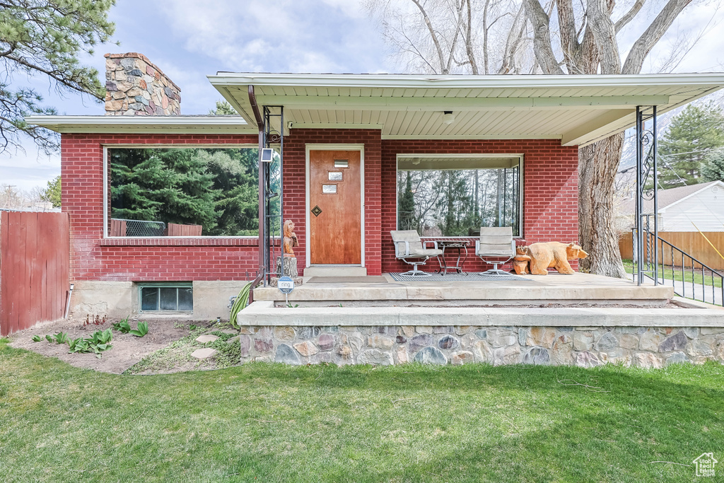 Doorway to property featuring a yard, covered porch, fence, brick siding, and a chimney