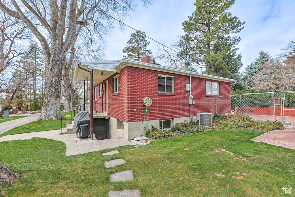 View of side of home featuring fence, cooling unit, a lawn, and a chimney