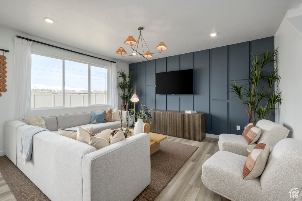 Living room with recessed lighting, a decorative wall, light wood-style floors, and an inviting chandelier