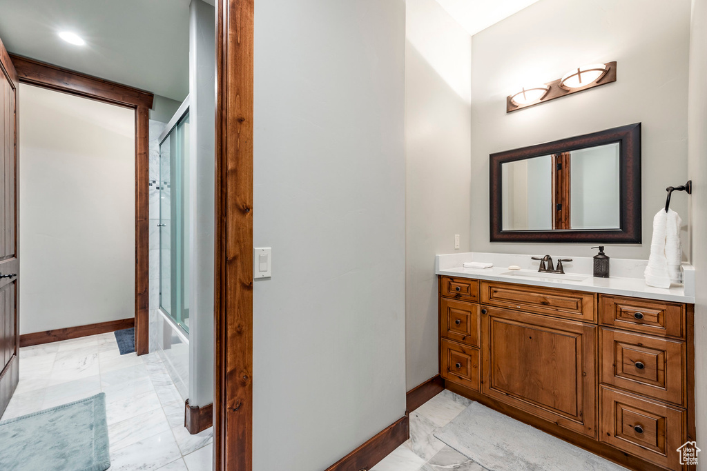 Full bath featuring baseboards, marble finish floor, vanity, and bath / shower combo with glass door
