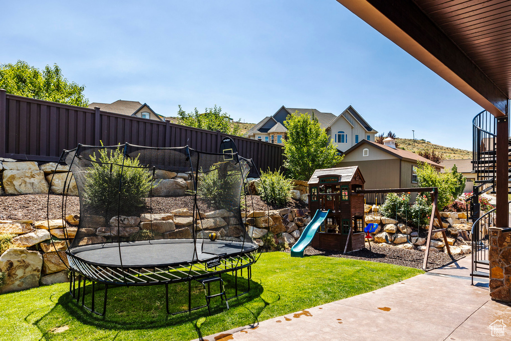 View of yard with a trampoline, fence, and a playground