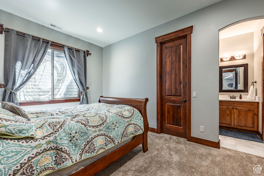 Bedroom featuring visible vents, baseboards, arched walkways, ensuite bath, and light carpet