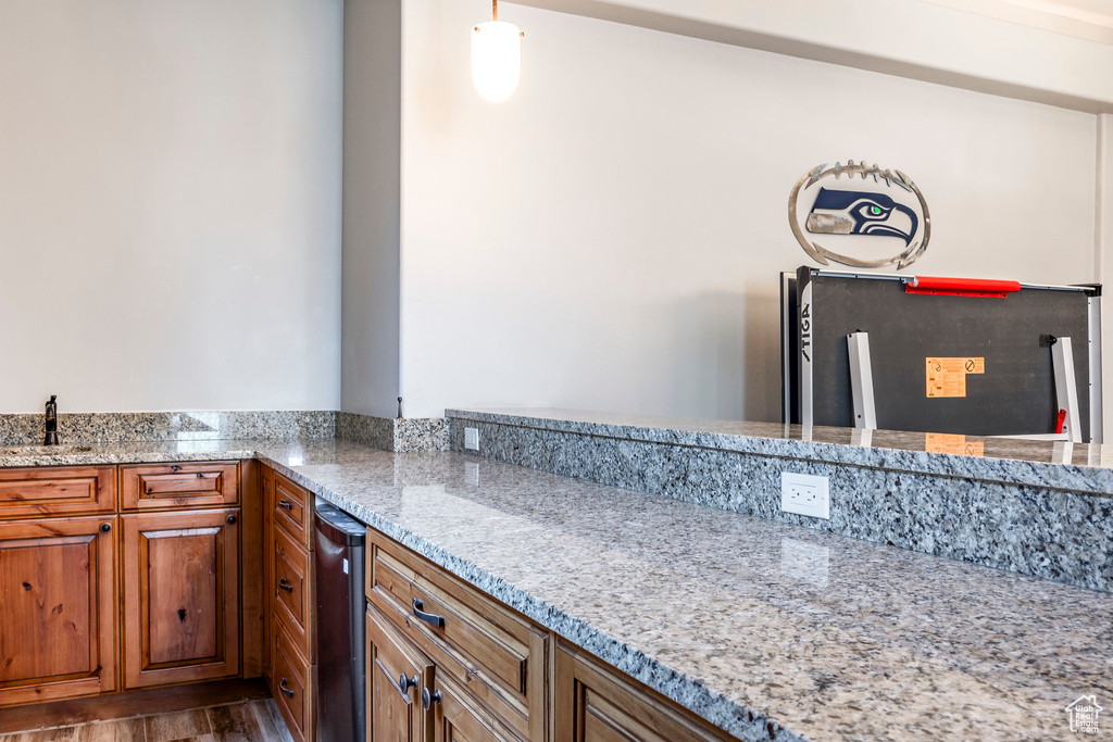 Kitchen featuring brown cabinets, wood finished floors, a sink, and light stone counters
