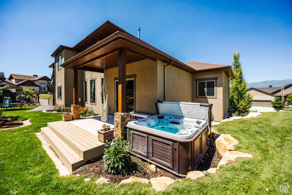Back of house with stucco siding, a wooden deck, a lawn, and a hot tub