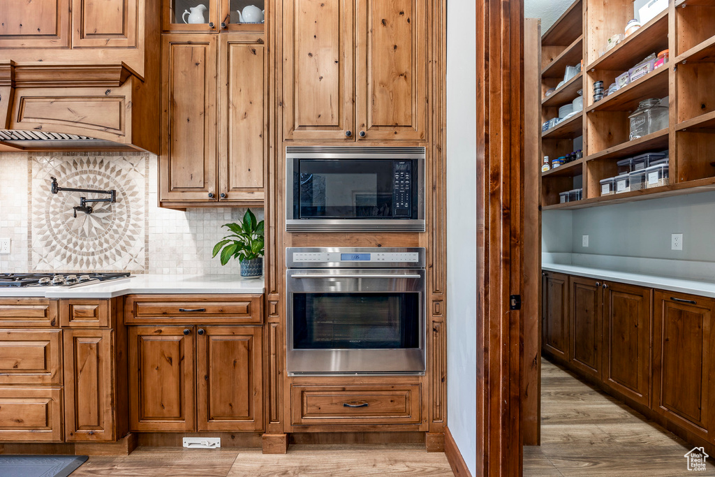 Kitchen featuring appliances with stainless steel finishes, light countertops, light wood finished floors, brown cabinets, and decorative backsplash