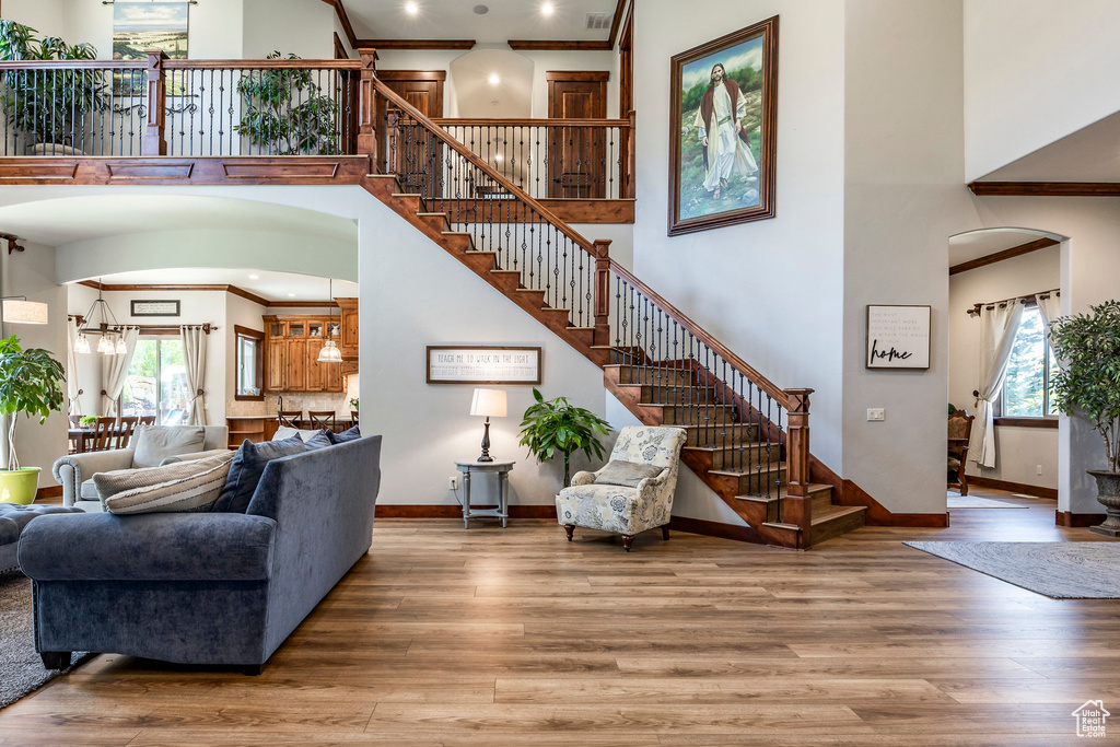 Living area featuring a towering ceiling, stairway, crown molding, arched walkways, and wood finished floors
