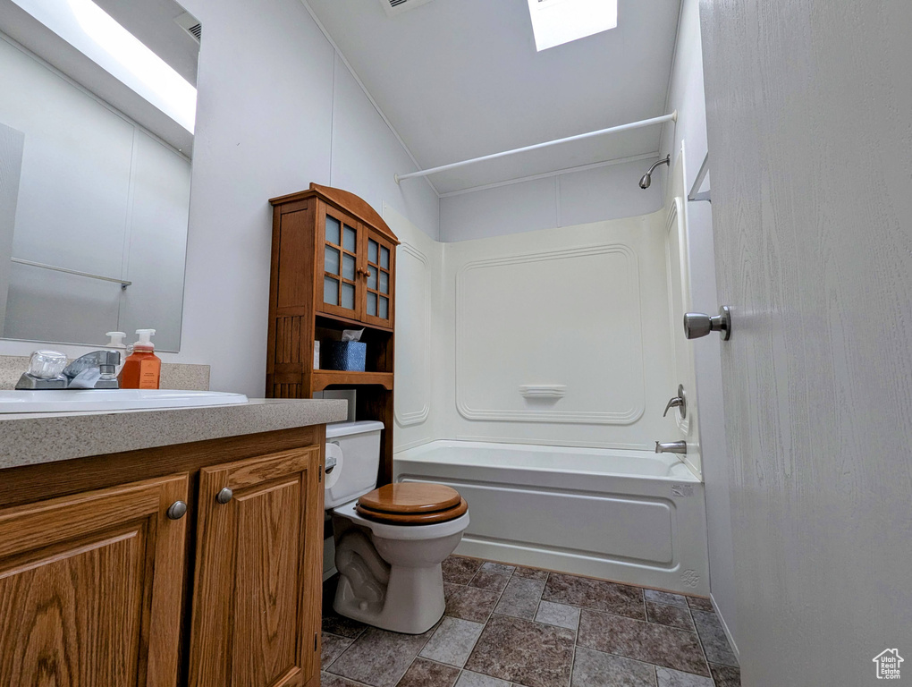 Full bath with toilet, stone finish floor, shower / bath combination, vanity, and a skylight