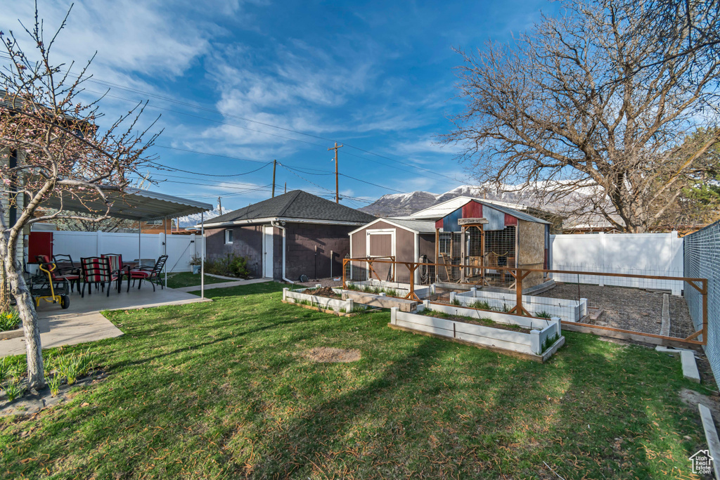 Back of house with an outbuilding, a fenced backyard, a lawn, a garden, and a patio