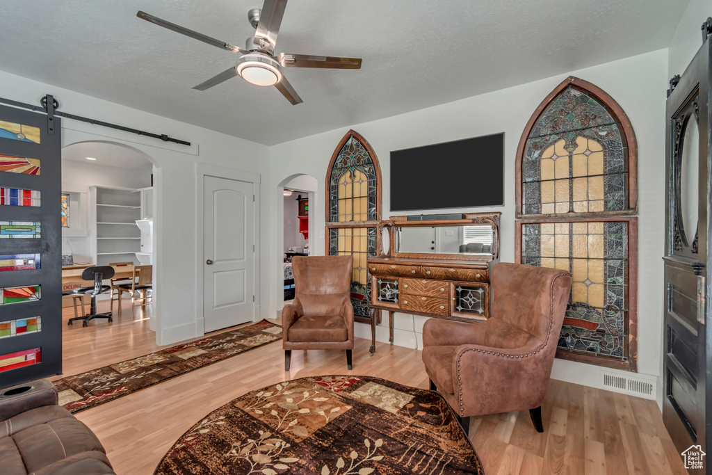 Living area featuring a ceiling fan, a barn door, visible vents, arched walkways, and wood finished floors