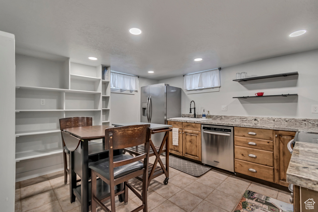 Kitchen featuring brown cabinetry, open shelves, light stone counters, a sink, and stainless steel appliances