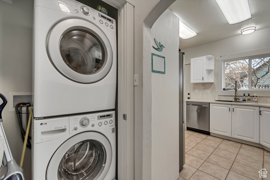 Washroom with light tile patterned floors, stacked washer / dryer, and a sink