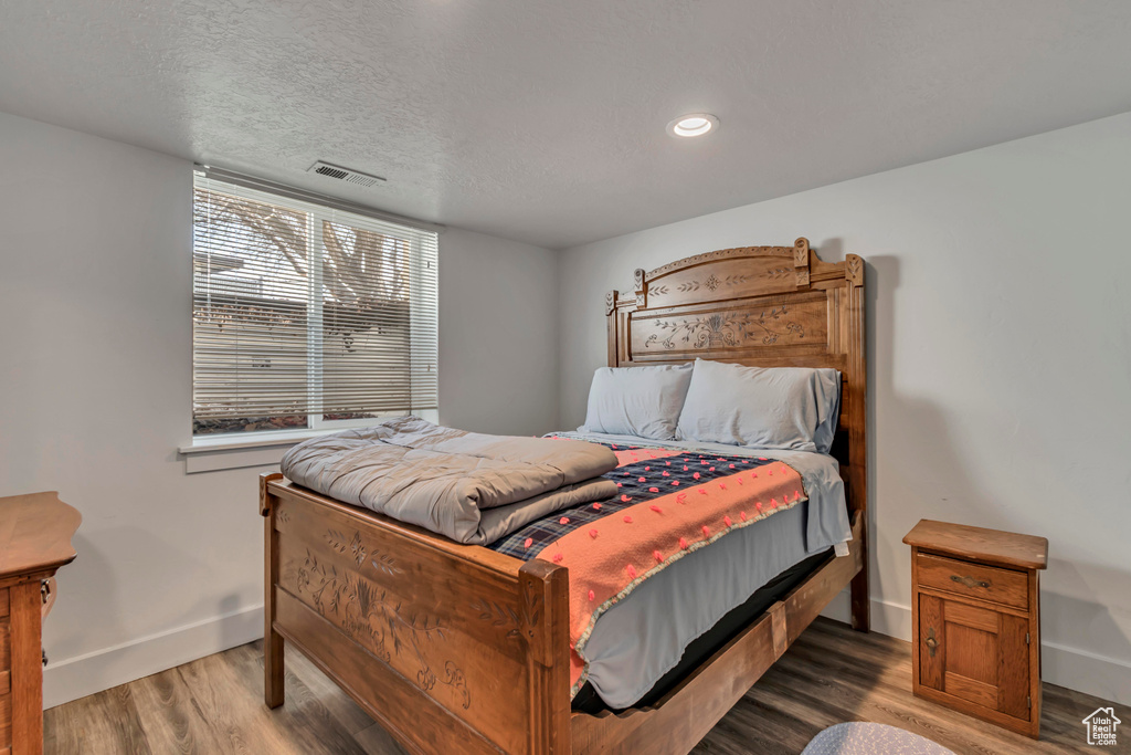 Bedroom with visible vents, baseboards, a textured ceiling, and wood finished floors