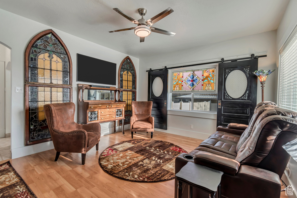 Living room with ceiling fan, arched walkways, a barn door, wood finished floors, and baseboards