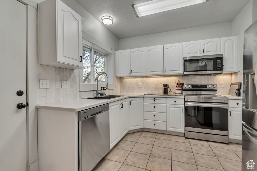 Kitchen with stainless steel appliances, light countertops, white cabinetry, and a sink