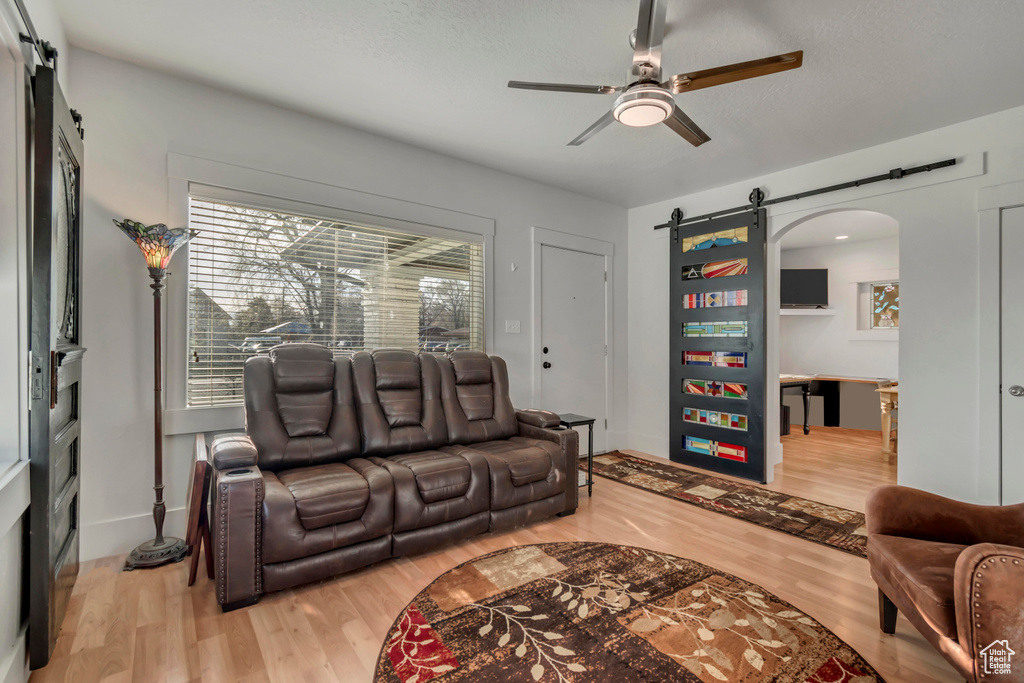 Living area with light wood finished floors, a ceiling fan, and a barn door