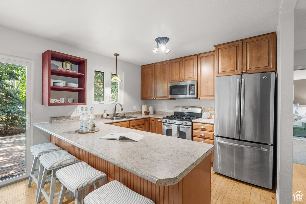Kitchen featuring appliances with stainless steel finishes, a peninsula, light countertops, and brown cabinetry