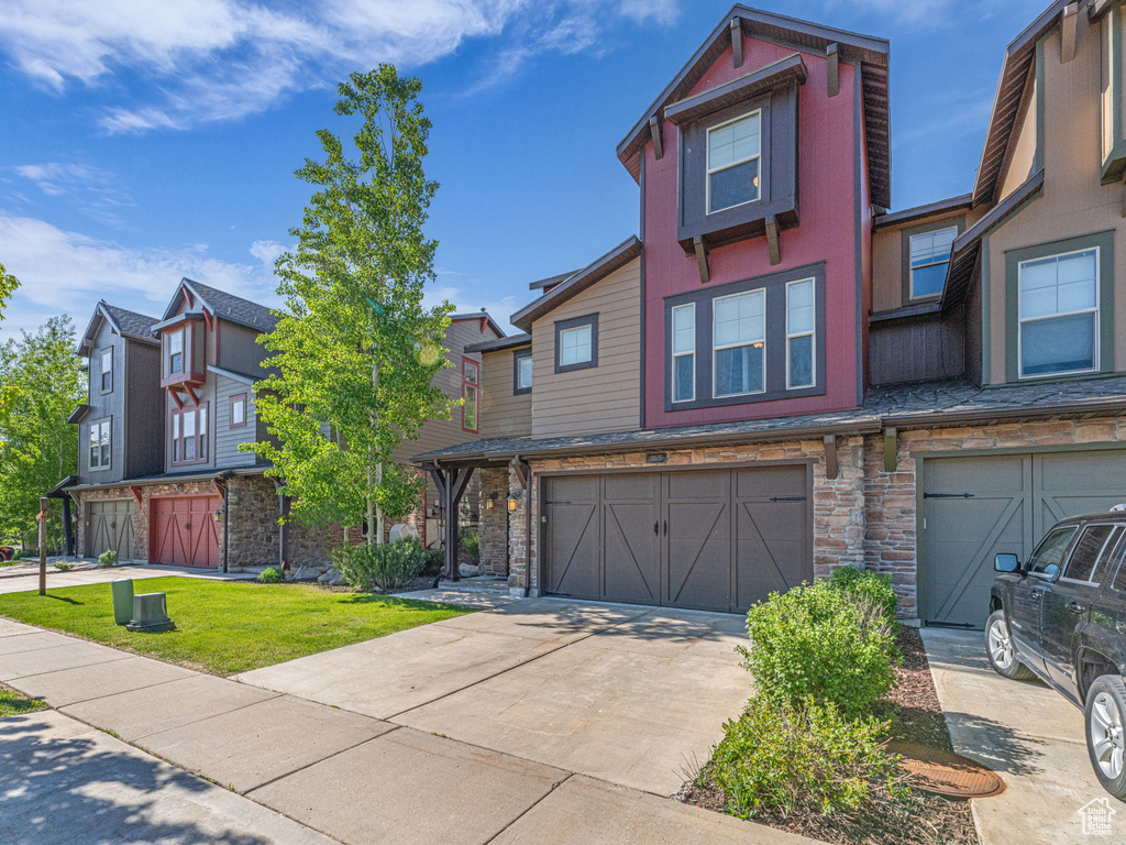 Townhome / multi-family property with an attached garage, driveway, stone siding, and a front yard