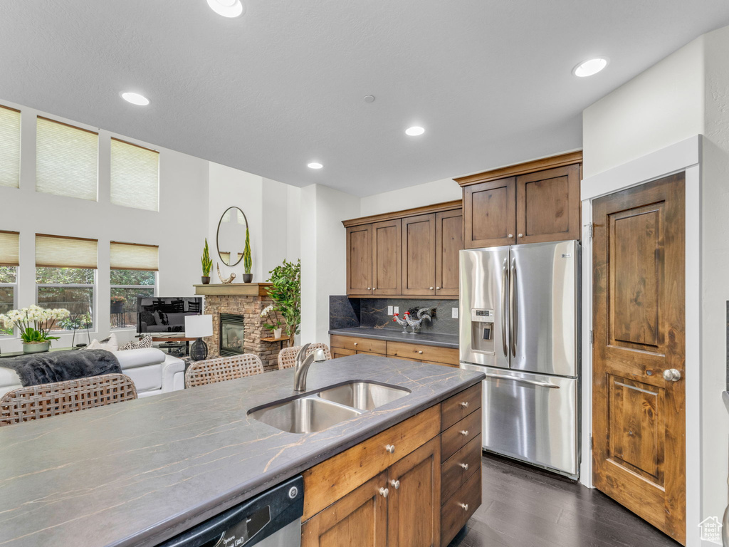 Kitchen with appliances with stainless steel finishes, a sink, a stone fireplace, dark wood-type flooring, and open floor plan