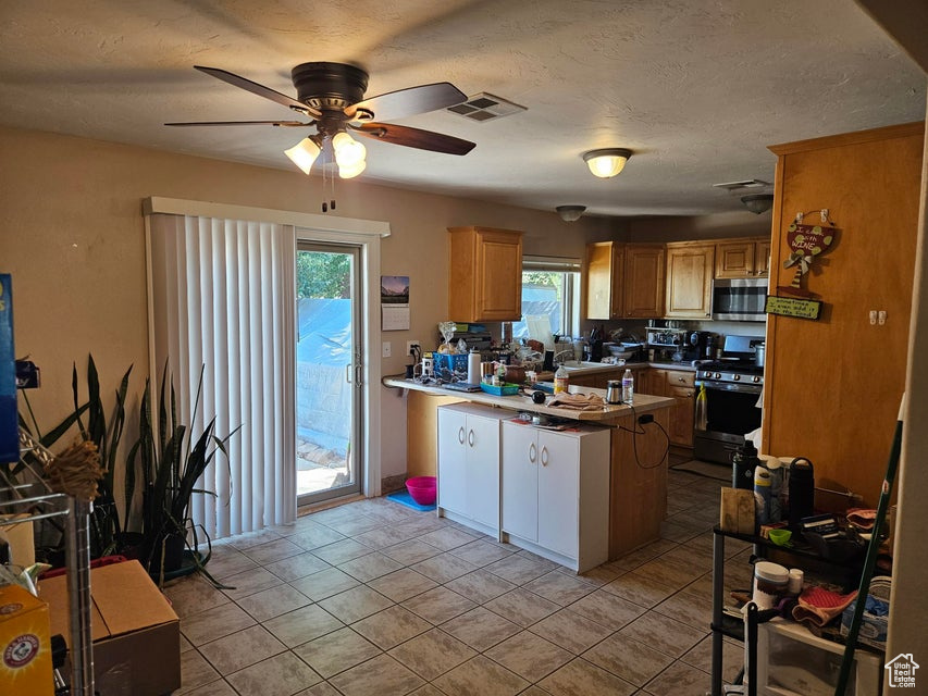 Kitchen featuring stainless steel appliances, a peninsula, a ceiling fan, plenty of natural light, and a textured ceiling