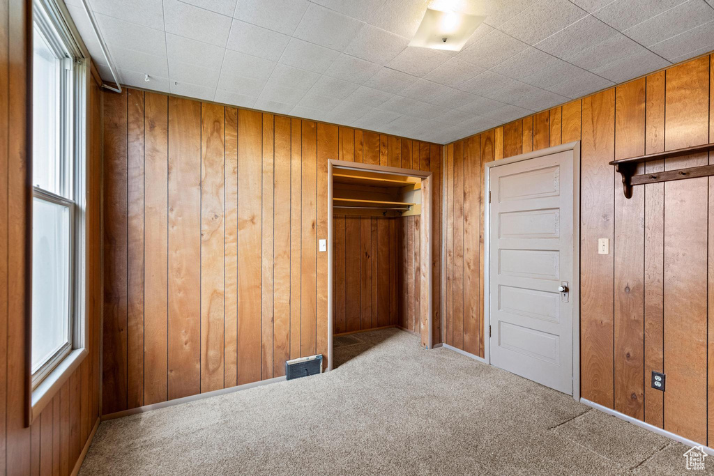 Unfurnished bedroom with carpet flooring, a closet, wooden walls, and visible vents