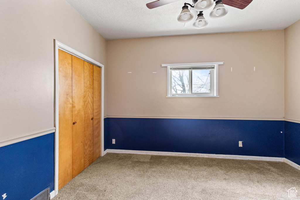 Carpeted empty room featuring visible vents, a textured ceiling, baseboards, and ceiling fan