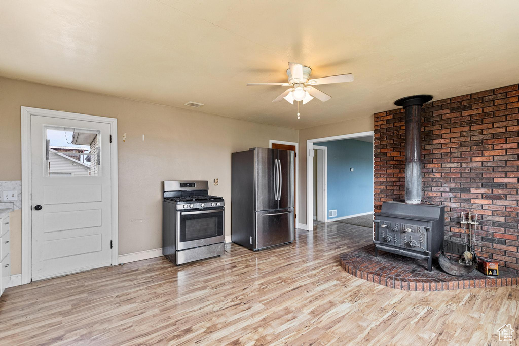 Kitchen featuring light wood finished floors, a wood stove, appliances with stainless steel finishes, baseboards, and ceiling fan