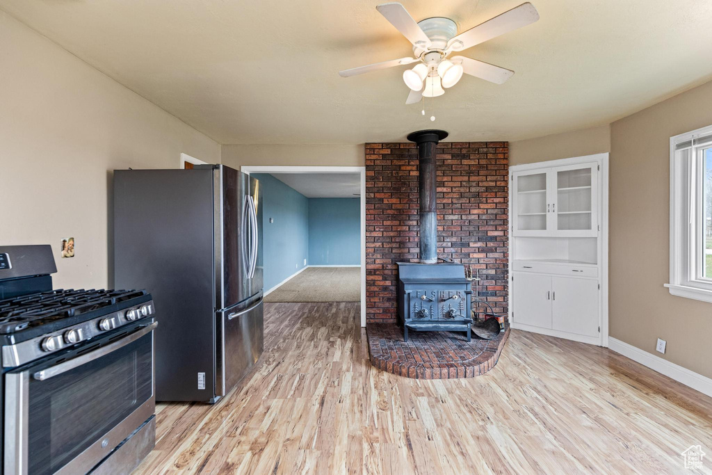 Kitchen with a wood stove, appliances with stainless steel finishes, baseboards, light wood-style floors, and ceiling fan