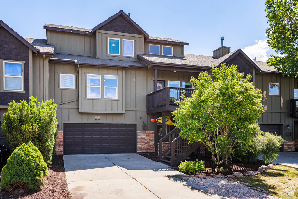 View of front facade with an attached garage, concrete driveway, a shingled roof, stairway, and stone siding
