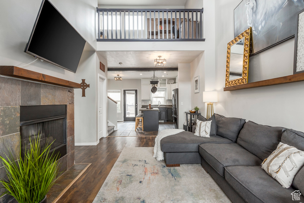 Living room featuring dark wood finished floors, baseboards, stairway, a high ceiling, and a tiled fireplace
